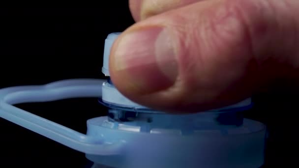 man unscrews the blue plastic cap of a large plastic water bottle on a black background. Garbage recycling concept - Metraje, vídeo