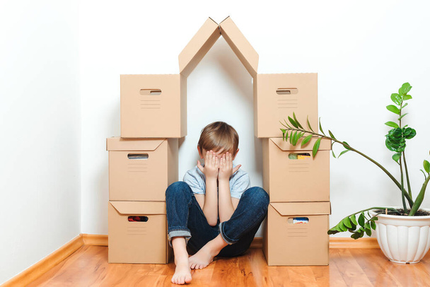Trauriges Kind versteckt sich im Haus und bastelt aus Schachteln. Hypotheken, Menschen, Wohnungen, Umzug und Immobilien. Kind träumt vom neuen Zuhause. Adoptionskonzept. - Foto, Bild