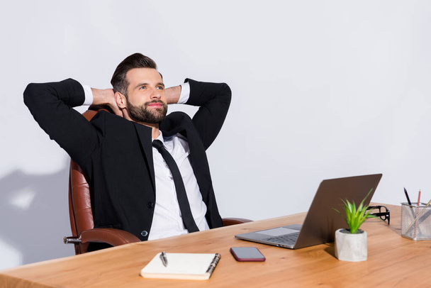 Photo of handsome cheerful business guy notebook table having break hands behind head look dreamy empty space wear black blazer shirt costume sit chair isolated grey background - Fotó, kép