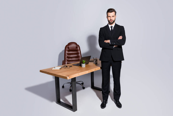 Full length photo of handsome macho business guy arms crossed strict chief look seriously not smile wear black blazer shirt pants shoes suit stand near table isolated grey background - Fotoğraf, Görsel