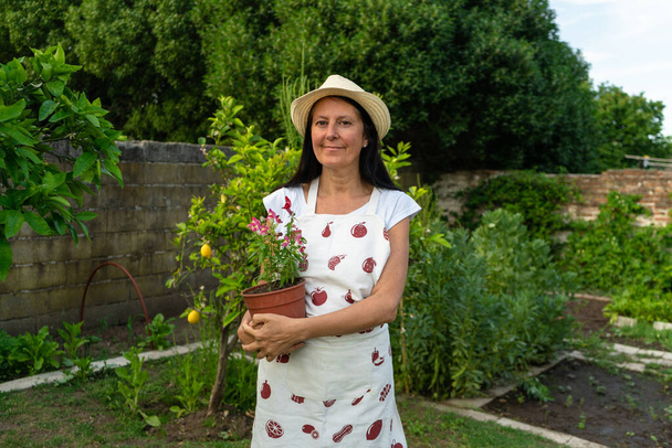 Женщина средних лет в саду держит цветочный горшок - Фото, изображение