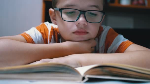 Dociekliwy, poważny chłopiec w okularach czyta ciekawą książkę w domu - Materiał filmowy, wideo