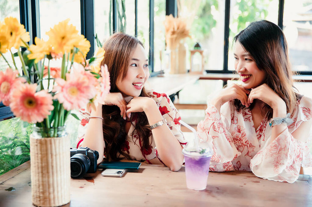 Kafede konuşan iki güzel ve mutlu kadın. Çiçekli cep telefonu içeceği ve masanın üstünde kamera. - Fotoğraf, Görsel