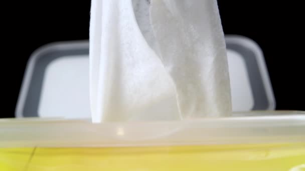 La salvietta umida monouso bianca è disegnata da una scatola di plastica gialla su uno sfondo nero. Il concetto di trattamento antivirale delle mani e delle superfici dai batteri del coronavirus. Macro sparato - Filmati, video