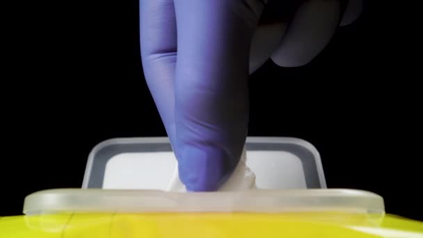 Hand in medical protective gloves takes a wet wipe for antibacterial disinfection. Yellow plastic pack. Virus protection measures, COVID-19. Close-up. On a black background. - Footage, Video