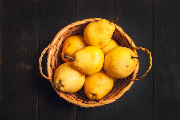 Natural pear fruit with defects in basket on dark wooden background. - Foto, Imagem