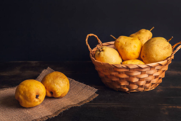 Natural pear fruit with defects in a basket on a jute napkin and a dark wooden background. - Foto, imagen