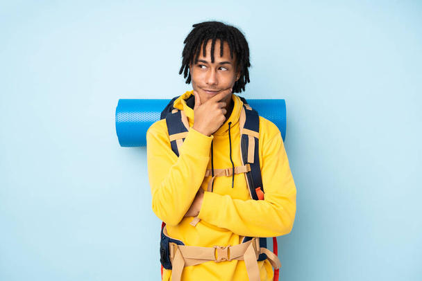 Young mountaineer african american man with a big backpack isolated on a blue background thinking an idea - Foto, imagen