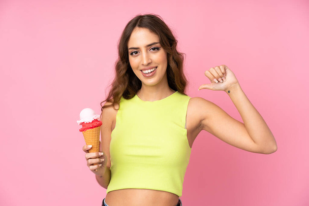 ピンクの背景に孤立した上にコルネットアイスクリームを保持若い女性誇りと自己満足 - 写真・画像