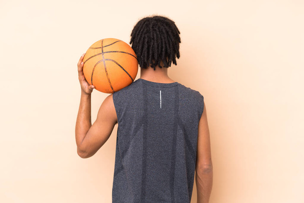 Young african american man isolated on beige background playing basketball in back position - Φωτογραφία, εικόνα