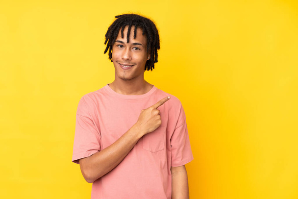 Jeune Afro-Américain isolé sur fond jaune pointant vers le côté pour présenter un produit - Photo, image