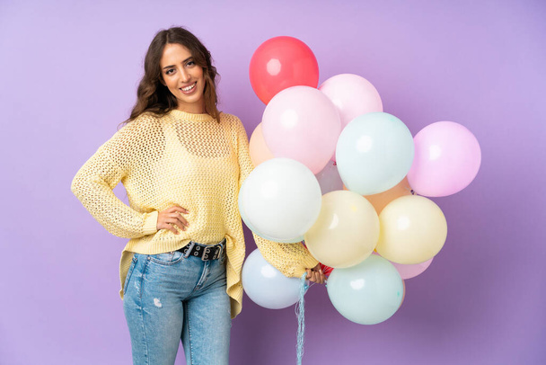 Young woman catching many balloons over isolated on purple background - Photo, Image