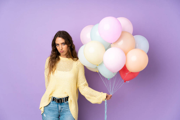 Junge Frau fängt viele Luftballons über isoliert auf lila Hintergrund flehend - Foto, Bild