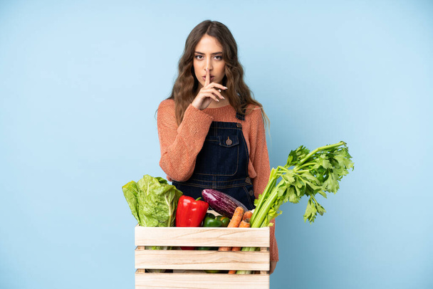 Rolnik ze świeżo zebranymi warzywami w pudełku ukazującym gest milczenia wkładający palec do ust - Zdjęcie, obraz