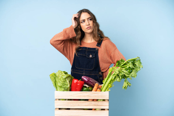 Fermier avec des légumes fraîchement cueillis dans une boîte ayant des doutes tout en grattant la tête - Photo, image