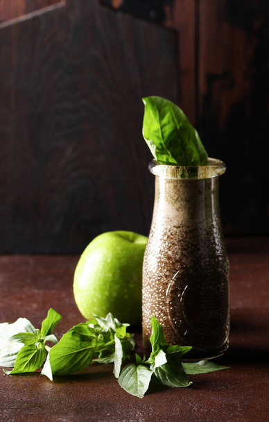 Detox and smoothies. Blueberry puree, berry juice, fresh spinach and apple in a clear basil bottle on a brown table. Rustic. Bar menu. Background image, copy space, vertical - Foto, immagini