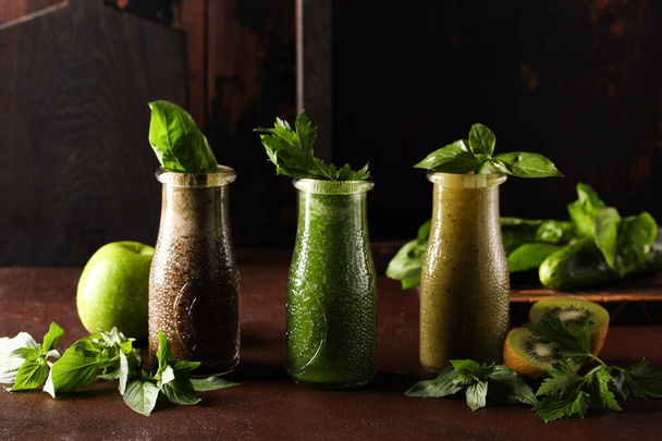 Smoothies and detox. Bottles of apple, kiwi, cucumber smoothies with herbs: parsley, basil, spinach and celery on a brown table. Rustic. Bar menu. Background image, copy space, horizontal - Foto, immagini