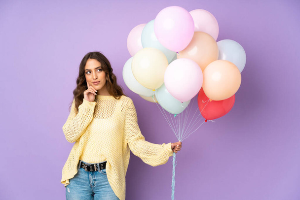Mladá žena chytání mnoho balónů nad izolované na fialovém pozadí myšlení nápad - Fotografie, Obrázek