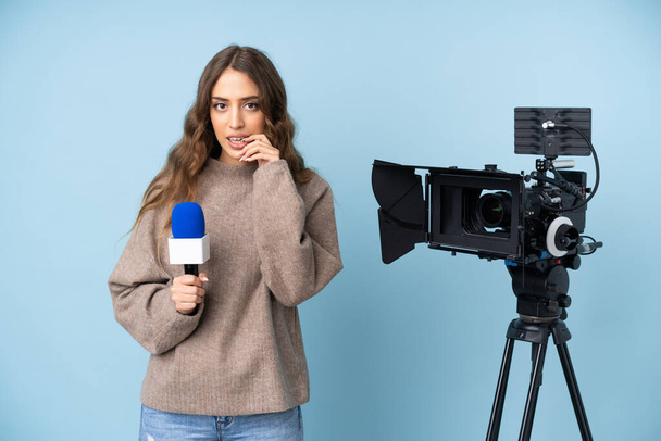 Δημοσιογράφος νεαρή γυναίκα κρατώντας ένα μικρόφωνο και αναφέροντας ειδήσεις νευρικές και φοβισμένη - Φωτογραφία, εικόνα