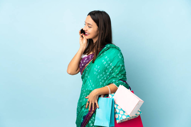 Jovem indiana com sacos de compras mantendo uma conversa com o telefone celular com alguém - Foto, Imagem