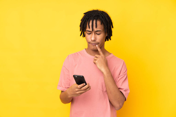 Молодий афроамериканець ізольований на жовтому фоні мислення і відправлення повідомлення - Фото, зображення