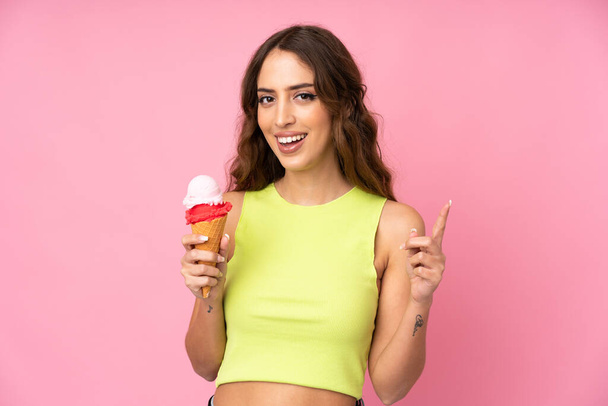 ピンクの背景に孤立した上にコーネットアイスクリームを保持している若い女性は素晴らしいアイデアを指摘 - 写真・画像