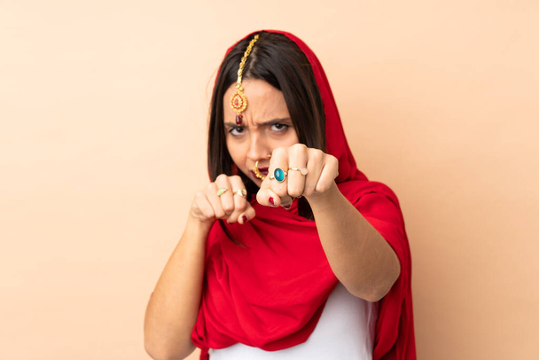 Young Indian woman isolated on beige background with fighting gesture - Фото, изображение
