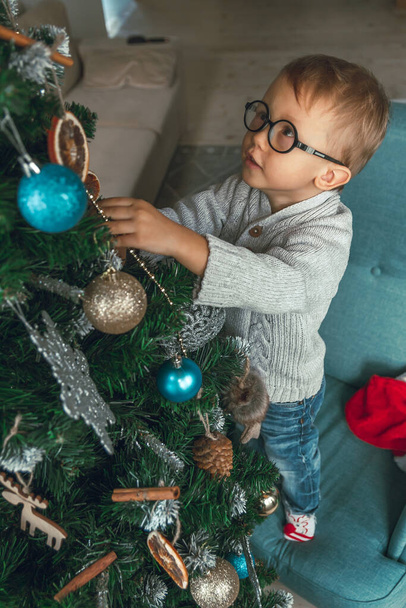 A Little boy decorates a Christmas tree - Foto, afbeelding