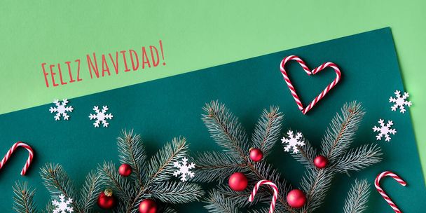 Christmas two tone festive background on green paper. Text Feliz Navidad means Merry Christmas in Spanish. Top view, panoramic banner image on fir twigs, red baubles, candy canes and snowflakes. - Photo, Image