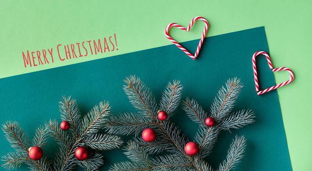 Christmas two tone festive background on green paper. Text Merry Christmas. Top view, panoramic banner image on fir twigs, red baubles, candy canes and snowflakes. - Foto, Bild