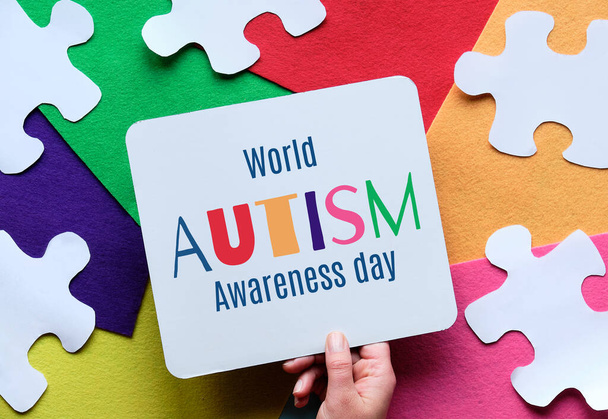 Hand holding caption for World Autism spectrum disorder Awareness Day on multicolor felt layered background with jigsaw pieces - Valokuva, kuva