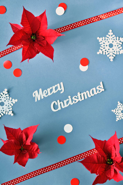 Text Merry Christmas. Top view on red decorations on grey paper. Trendy geometric background with long shadows. Poinsettia, paper snowflakes, dual-color paper confetti. - Fotografie, Obrázek