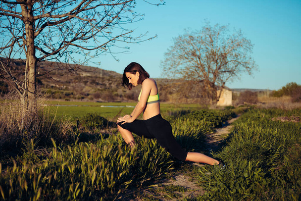 Vrouwelijke loper stretching buiten in het veld voor de oefening - Foto, afbeelding