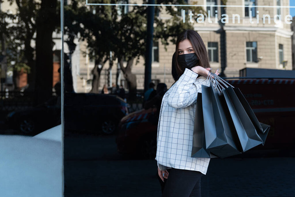 Junge Frau in schwarzer Arztmaske hält Pakete zum Einkaufen auf schwarzem Hintergrund. Einkaufen während der Quarantäne - Foto, Bild
