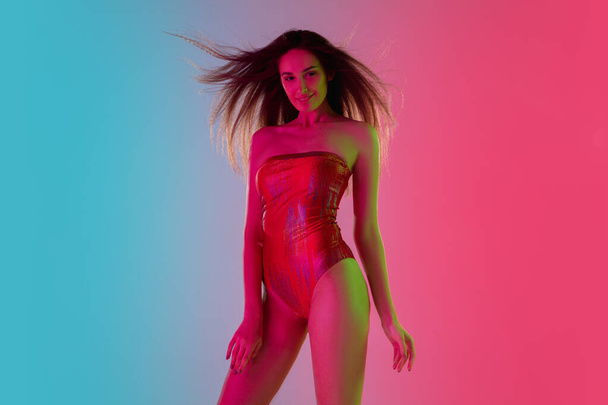 Beautiful seductive girl in fashionable red swimsuit on bright gradient pink-blue background in neon light - Foto, Imagem