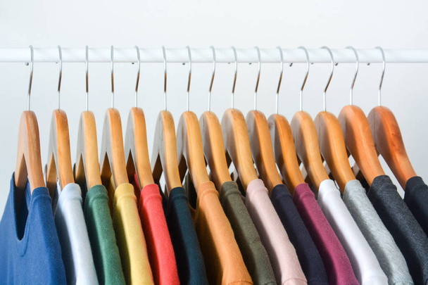 закрыть коллекцию разноцветных футболок, висящих на вешалке из деревянной одежды в шкафу или вешалке для одежды на белом фоне - Фото, изображение