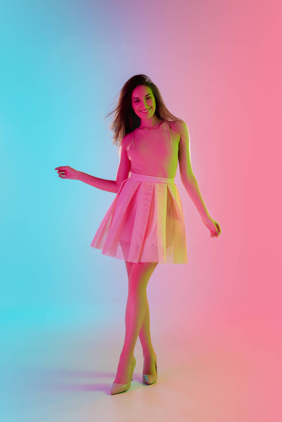 Beautiful seductive girl in fashionable, romantic outfit on bright gradient pink-blue background in neon light - Fotó, kép