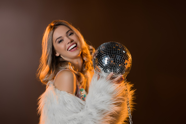 happy blonde woman in faux fur jacket holding disco ball on black  - Photo, Image