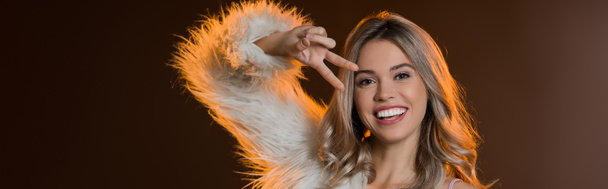 pleased blonde woman in faux fur jacket showing peace sign on black, banner - Photo, Image