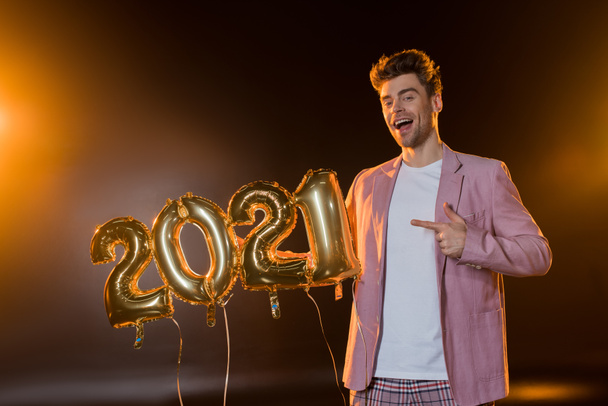 cheerful man pointing with finger at 2021 numbers balloons on black  - Photo, Image