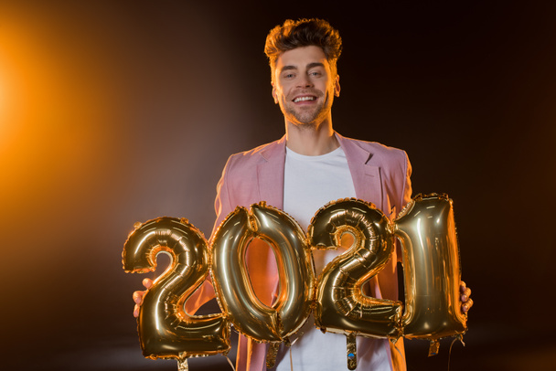 cheerful man holding 2021 numbers balloons on black  - Fotografie, Obrázek