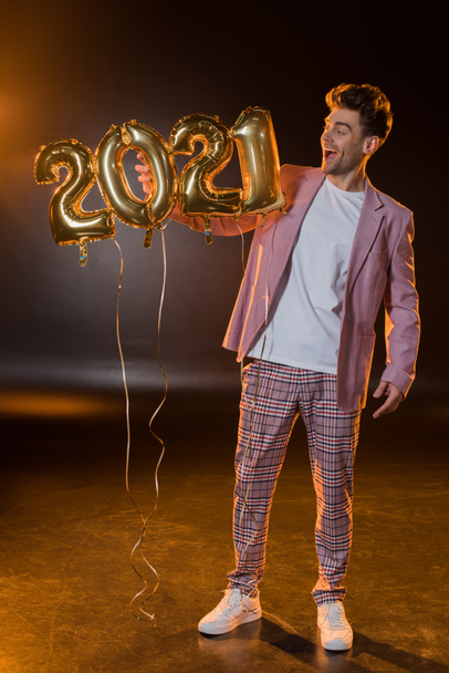 full length of cheerful man holding 2021 numbers balloons on black  - Fotó, kép
