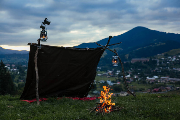 山の中で夜に屋外でキャンプテントの近くにたき火。日没後の提灯や火でピクニック - 写真・画像