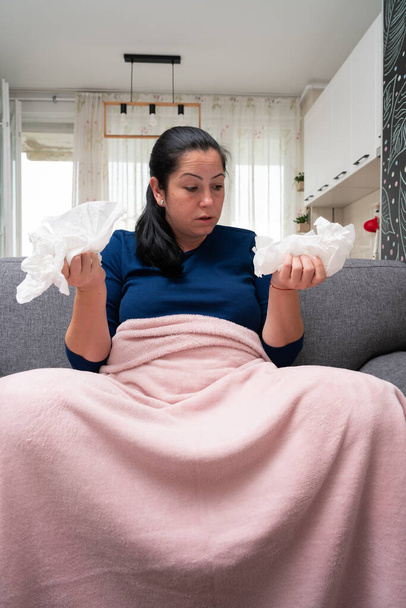 Studená dospělá žena necítí dobře při pohledu na použité ubrousky v rukou s sars covid sinusitis příznaky sedí na pohovce doma - Fotografie, Obrázek
