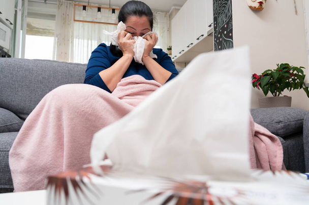 Selektywne zbliżenie ostrości na opakowaniu serwetek na stole z chorą dorosłą kobietą dmuchającą zatkany nos w tle z objawami przeziębienia lub grypy - Zdjęcie, obraz
