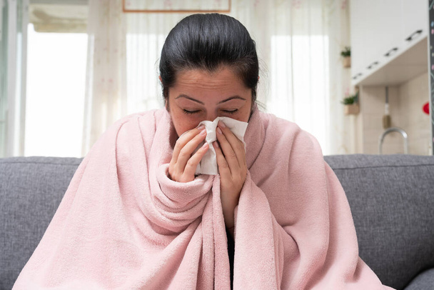 Sick adult female model on sofa blowing stuffy nose as sinusitis concept having sars covid flu influenza symptoms - Foto, immagini