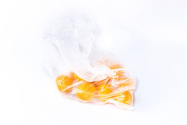 Ripe orange tangerines in closed plastic cellophane bag on a white background. Ecology concept - 写真・画像