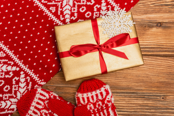 top view of gift box and red knitted scarf and mittens on wooden background - Fotoğraf, Görsel