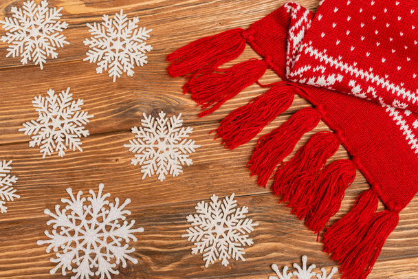 top view of winter snowflakes and red knitted scarf on wooden background - Photo, image