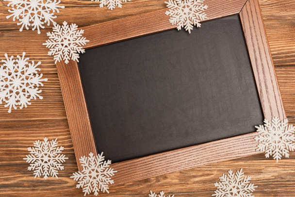top view of winter snowflakes on chalkboard on wooden background - Foto, imagen